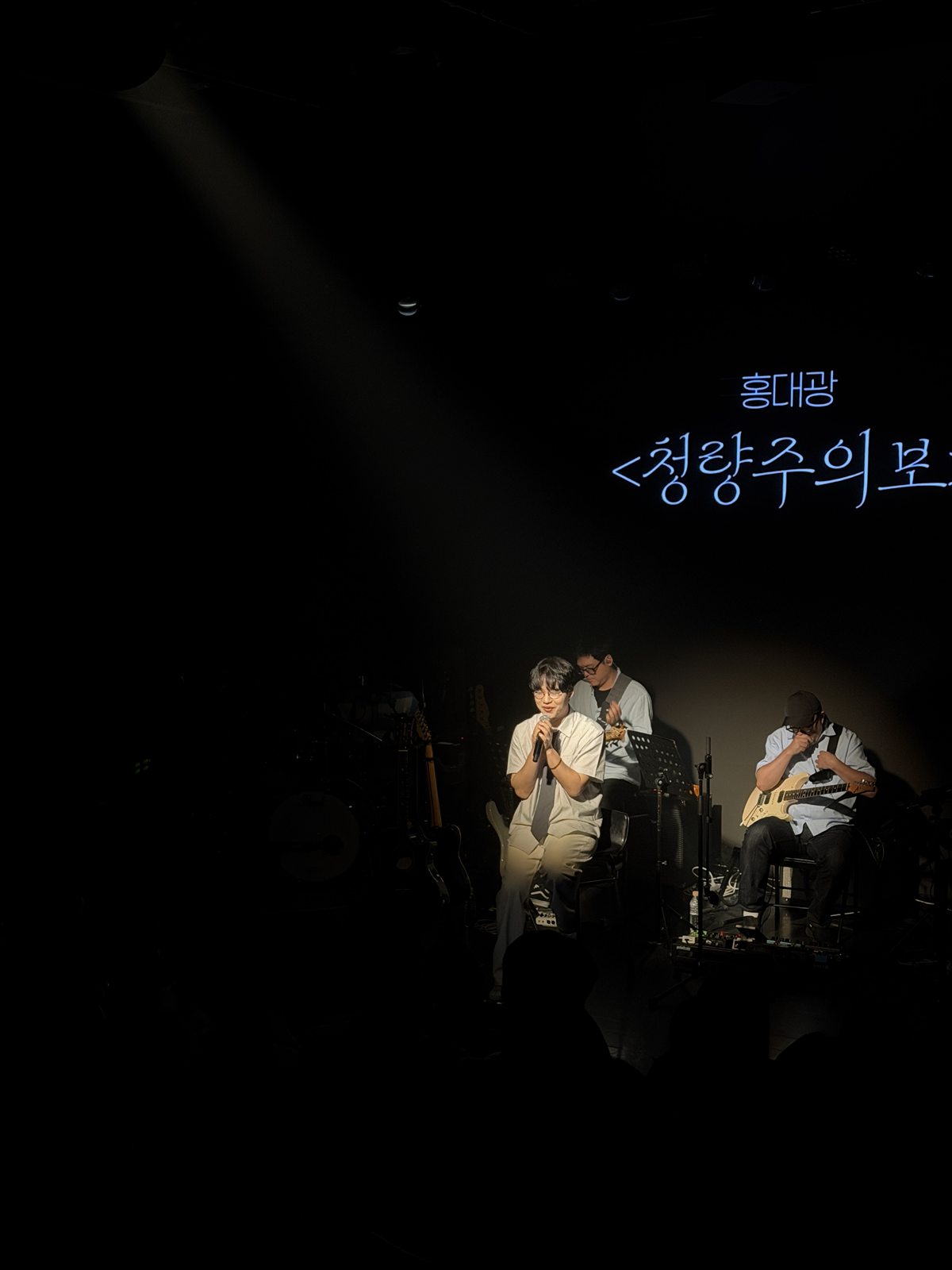 어두운 무대 위 스포트라이트를 받으며 노래하는 홍대광, 뒤로 보이는 '청량주의보' 타이틀
