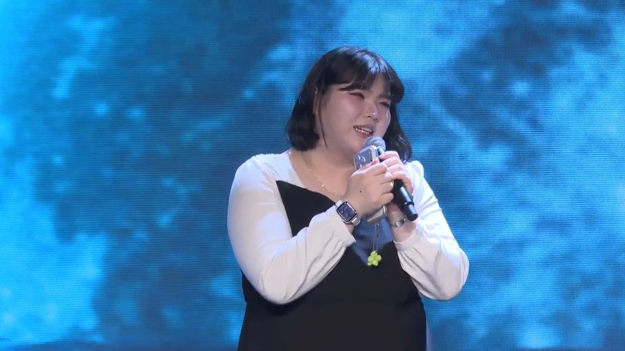 온맘씨어터 프리즘 미니콘서트 — 푸른 LED 스크린 앞에서 마이크를 두 손으로 잡고 노래하는 출연자