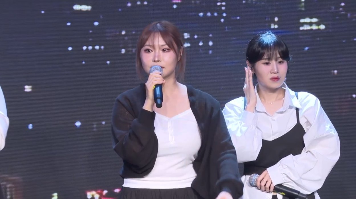 온맘씨어터 프리즘 미니콘서트 — 도시 야경 LED 영상 앞에서 마이크를 들고 이야기하는 출연자들