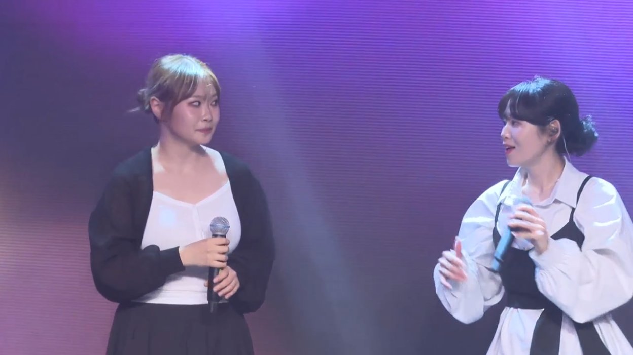 온맘씨어터 프리즘 미니콘서트 — 무대 위에서 마이크를 들고 마주 보며 대화하는 두 출연자