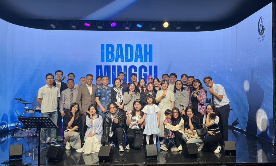 'IBADAH MINGGU(주일 예배)' 화면이 띄워진 온맘씨어터 무대에서 찍은 하티엘룩 교회 성도 단체 사진